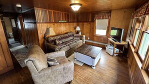 L’intérieur chaleureux d’un chalet avec un canapé, une table basse, un téléviseur et des murs en bois.