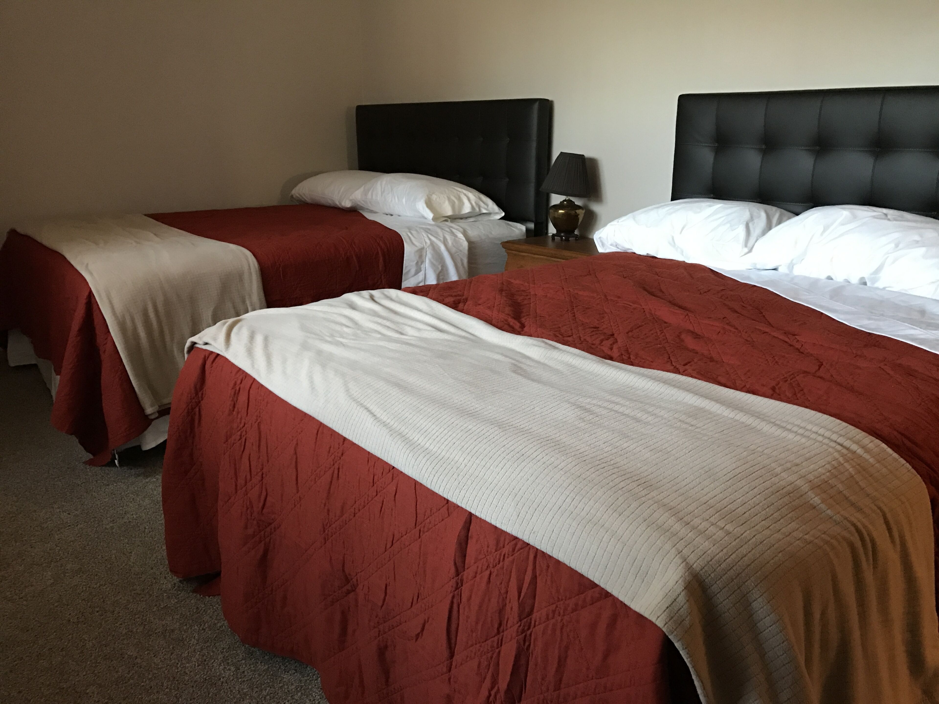 Ein Hotelzimmer mit zwei Betten, jeweils mit einer roten und weißen Bettdecke, einem schwarzen Kopfteil und einem Nachttisch mit einer Lampe.