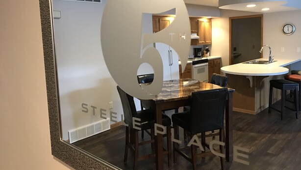 A modern kitchen with a central island, wooden chairs, and a built-in oven. - 5th Steele Place, LLC - Downtown Algoma Condos: Overnight or Extended Stays (Algoma)