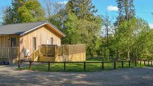 A wooden cabin with a porch and a fenced deck, surrounded by trees and a clear sky. - 3 bedroom accommodation in Otterburn, near Bellingham (Otterburn, near Bellingham)