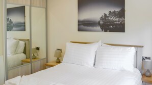 A neatly made bed with white linens and a folded towel, a bedside lamp, and a framed picture of a forest on the wall. - 3 bedroom accommodation in Otterburn, near Bellingham (Otterburn, near Bellingham)