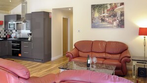 A modern living room with a leather sofa, a dining table, and a kitchen area with grey cabinets and a microwave. - 3 bedroom accommodation in Otterburn, near Bellingham (Otterburn, near Bellingham)