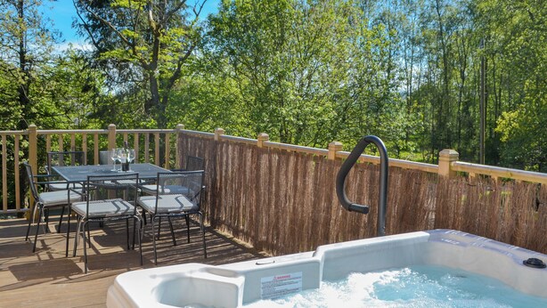 A hot tub on a wooden deck with a table and chairs, surrounded by a wooden fence and trees. - 3 bedroom accommodation in Otterburn, near Bellingham (Otterburn, near Bellingham)