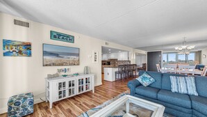 A spacious living room with a blue sofa, a white cabinet, and a framed picture of a beach scene. - The Quay 2102 by Seaside Vacations & Sales (Ocean City)