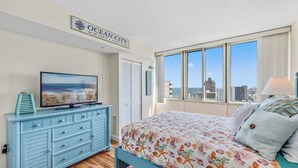A bedroom with a large bed, a TV on a dresser, a city view, and a sign reading "Ocean City". - The Quay 2102 by Seaside Vacations & Sales (Ocean City)
