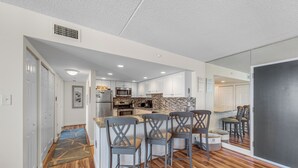 A modern kitchen with white cabinets, a central island with bar stools, and a stone backsplash. - The Quay 2102 by Seaside Vacations & Sales (Ocean City)