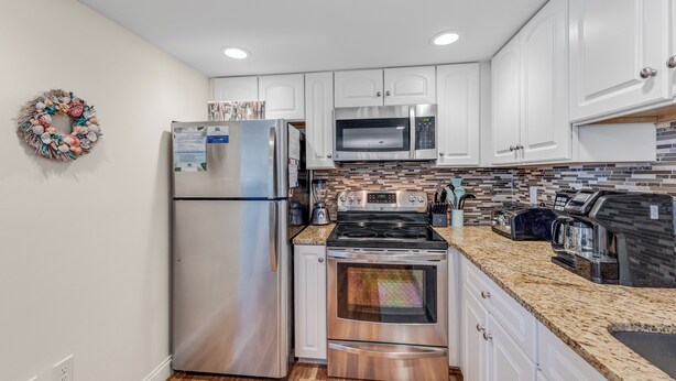 A modern kitchen with stainless steel appliances, white cabinetry, and a herringbone tile backsplash. - The Quay 2102 by Seaside Vacations & Sales (Ocean City)