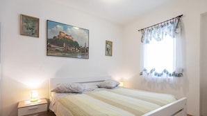 Een slaapkamer met een bed, een nachtkastje, een raam met gordijnen en twee ingekaderde foto's aan de muur.