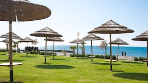 Een strandgedeelte met rieten parasols en tafels, een helder uitzicht op de zee, en een pad dat naar het strand leidt.