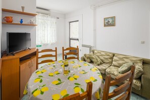 A compact living space with a dining table, chairs, a sofa, a TV, and a radiator. - Comfortable two bedroom apartment in a top location in Porec near the beach with a private terrace in the garden (Porec)