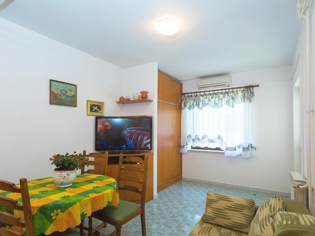 A living room with a television, a dining table with a tablecloth, a sofa, and a window with curtains.