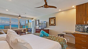 Habitación de hotel con una cama grande, un escritorio pequeño, kitchenette y vista al océano.