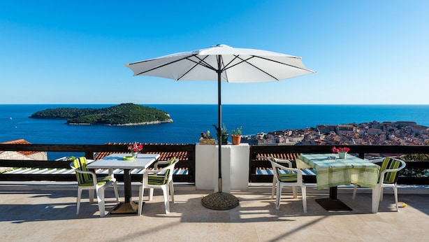 A terrace with a table and chairs, a large umbrella, and a view of the sea and a distant island. - Guesthouse Home Sweet Home - Double Room with Shared Terrace (Dubrovnik)