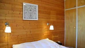 Habitación con paredes de paneles de madera, una cama con ropa blanca, dos lámparas fijadas a la pared y un cuadro enmarcado sobre la cama.