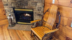 A stone fireplace with a fire, a wooden chair with metal legs, and a small decorative figure. - A Painted Pony - Cabin (Sevierville)