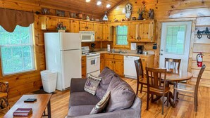A cozy cabin-style kitchen with wooden cabinets, a refrigerator, stove, and a dining area with a table and chairs. - A Painted Pony - Cabin (Sevierville)