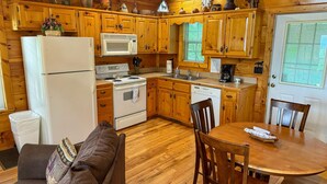 A compact kitchen with wooden cabinets, a refrigerator, stove, microwave, and dishwasher. There is a dining table with chairs and a small sofa in the corner. - A Painted Pony - Cabin (Sevierville)
