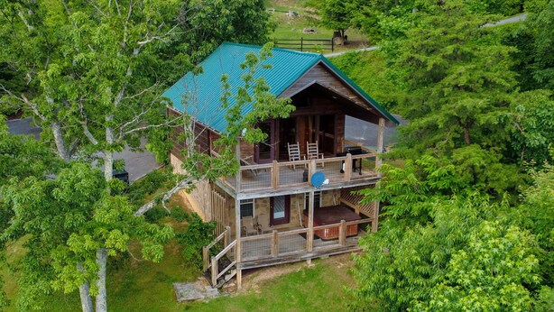 A two-story cabin with a green roof, surrounded by dense forest. - Angel's View By Volunteer Cabin Rentals - Cabin In The Smokies (Sevierville)