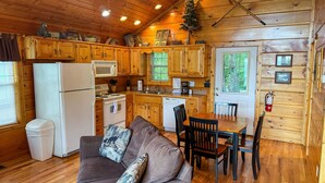 A cozy cabin-style kitchen with wooden cabinets, a refrigerator, stove, and a dining area with a table and chairs. - Angel's View By Volunteer Cabin Rentals - Cabin In The Smokies (Sevierville)