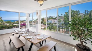 A dining area with a table set for four, large windows offering a view of the sea and surrounding buildings. - Villa Jimena by Mabiente Properties by Mabiente Properties (Mijas)