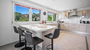 A modern kitchen with a central island, bar stools, and large windows offering a view of the landscape. - Villa Jimena by Mabiente Properties by Mabiente Properties (Mijas)