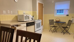 Une cuisine compacte équipée d’un four à micro-ondes, d’un four traditionnel et d’un lave-vaisselle. On y trouve une table à manger avec deux chaises et une fenêtre avec des stores.
