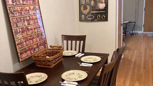 Un coin repas avec une table en bois dressée pour quatre personnes, entourée de chaises. Un poster encadré est accroché au mur, à gauche, et une image encadrée se trouve au-dessus de la table.