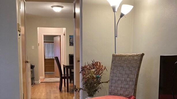 Un couloir avec un plancher en bois, une chaise en osier avec un coussin rouge, un lampadaire et un téléviseur posé sur une table.