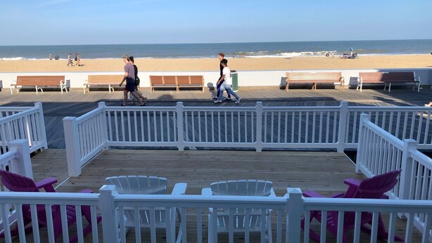 A wooden deck with white railings and purple chairs, overlooking a beach with benches and people. - Beach Cottage 1Bed & 1Bath Fully Renovated next to the Boardwalk (Ocean City)