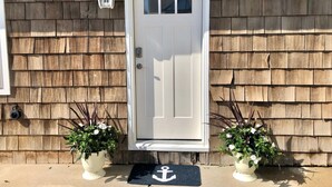 A white front door with a small window above it, flanked by two potted plants with white flowers. - Beach Cottage 1Bed & 1Bath Fully Renovated next to the Boardwalk (Ocean City)
