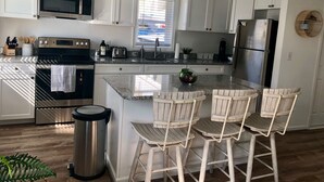A modern kitchen with white cabinets, stainless steel appliances, a granite countertop, and a central island with bar stools. - Beach Cottage 1Bed & 1Bath Fully Renovated next to the Boardwalk (Ocean City)