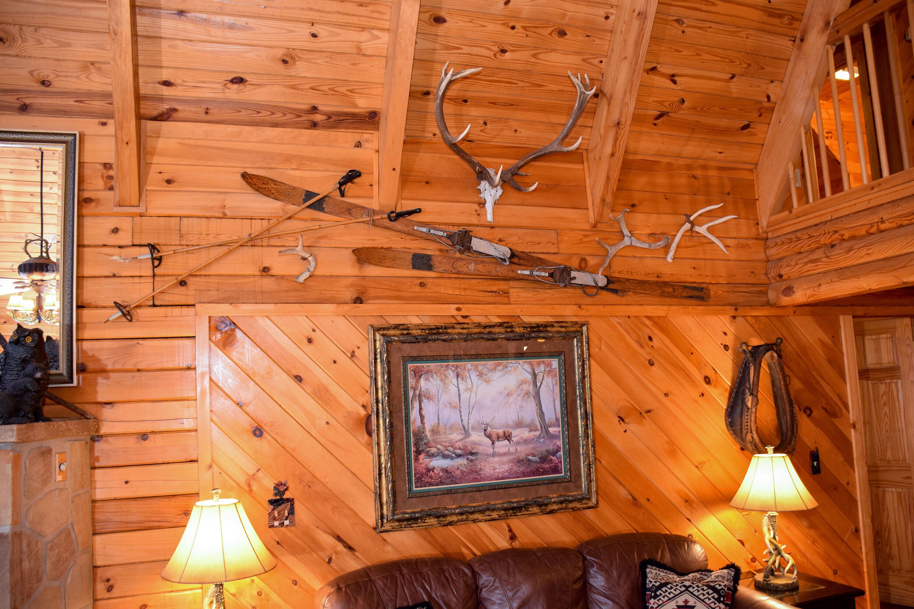 A wooden interior with a framed deer painting, a brown leather couch, and mounted antlers.