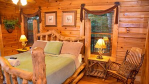 A log cabin bedroom with a wooden bed, two bedside lamps, a rocking chair, and framed pictures on the wall. - Grand Vista Lodge - Cabin (Sevierville)