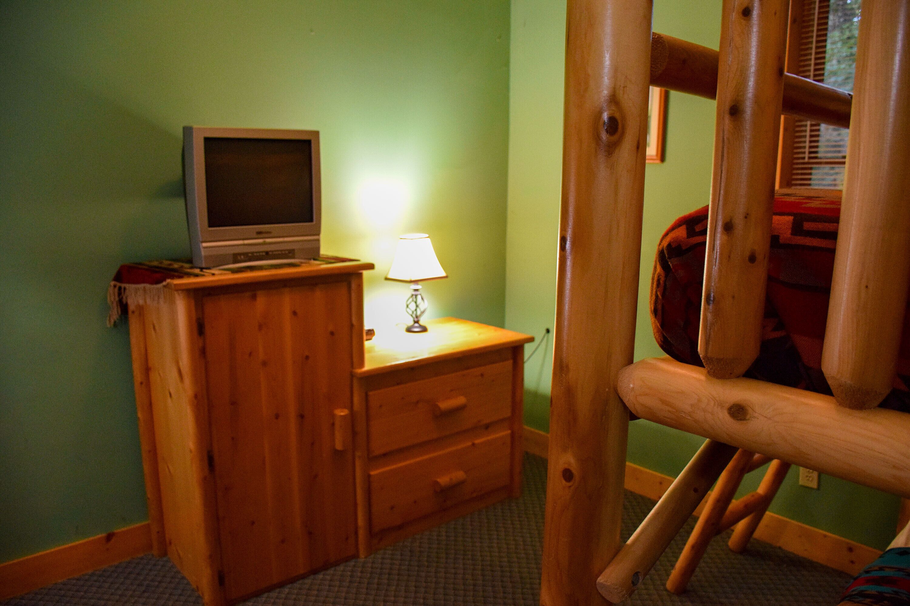 A room with a wooden dresser, a television on top, and a lamp on the dresser.