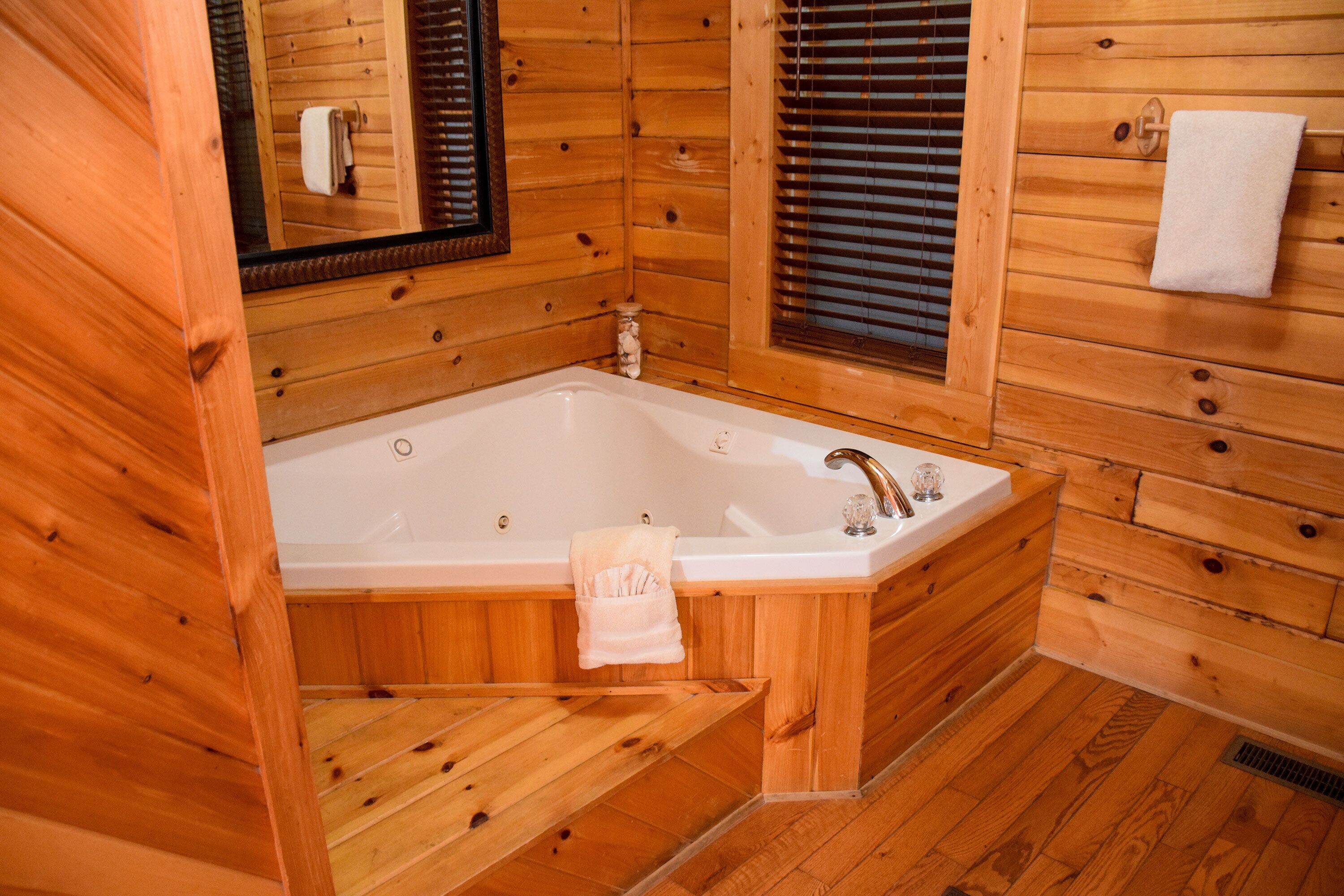 A wooden cabin bathroom with a bathtub, wooden walls, and a window with blinds.