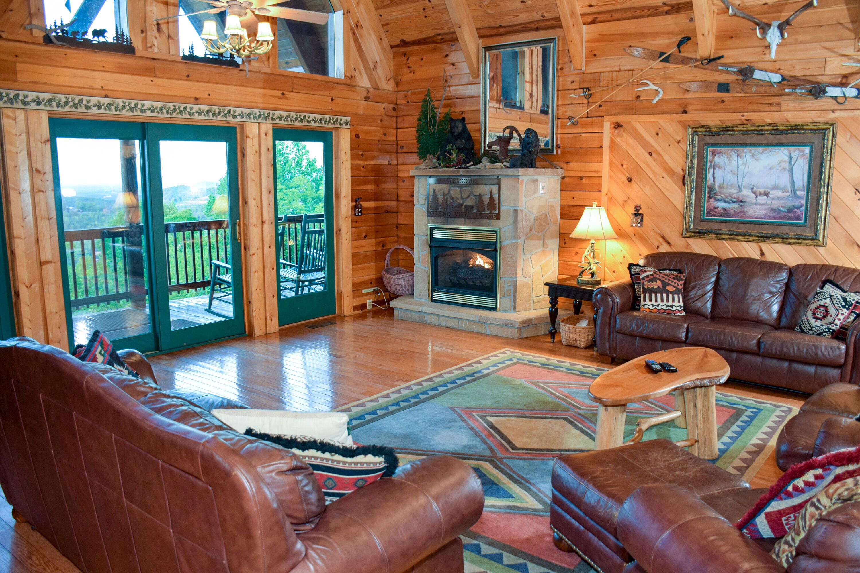 A log cabin interior with a fireplace, leather furniture, and a balcony with a view.