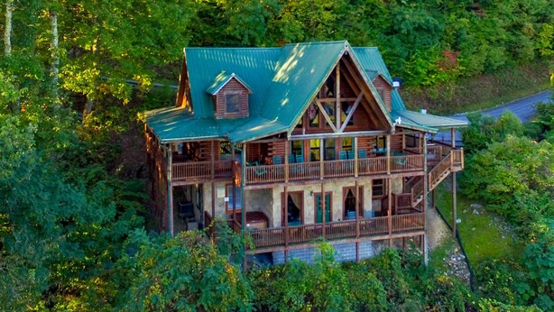 A multi-story log cabin with a green roof, surrounded by dense forest. - Grand Vista Lodge - Cabin (Sevierville)