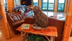 A wooden cabin interior with a brown leather sofa, a wooden table with a magazine, and a bear sculpture. - Grand Vista Lodge - Cabin (Sevierville)