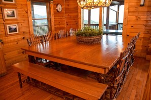 A wooden dining table with benches, surrounded by wooden walls and a large window.