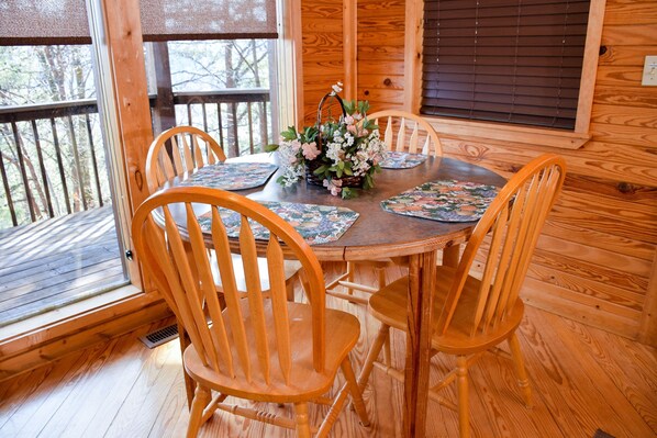 A wooden dining table with four chairs, a floral centerpiece, and a window with blinds. - Hiker's Point - Cabin In The Smokies (Sevierville)