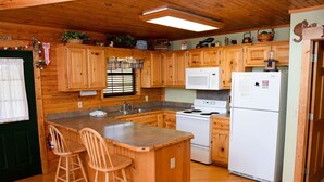 A cabin-style kitchen with wooden cabinets, a central island with stools, a stove, a microwave, and a refrigerator. - Hiker's Point - Cabin In The Smokies (Sevierville)