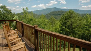 A wooden deck with chairs overlooking a forested mountain range. - Hiker's Point - Cabin In The Smokies (Sevierville)