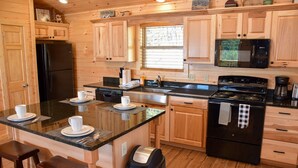 A kitchen with wooden cabinets, a black refrigerator, a microwave, a stove, and a coffee maker. - Little Feather - 1 Level Cabin (Sevierville)