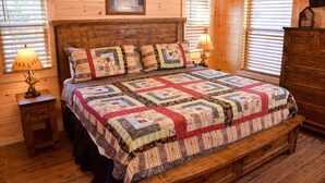 A wooden cabin bedroom with a large bed, two bedside tables with lamps, a wooden dresser, and a window with blinds. - Little Feather - 1 Level Cabin (Sevierville)