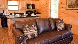 A brown leather sofa with animal-themed cushions, a wooden kitchen with a microwave, and a framed picture on the wall. - Little Feather - 1 Level Cabin (Sevierville)