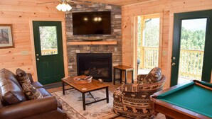A cozy cabin interior with a fireplace, a pool table, a leather sofa, and a television mounted on the wall. - Little Feather - 1 Level Cabin (Sevierville)