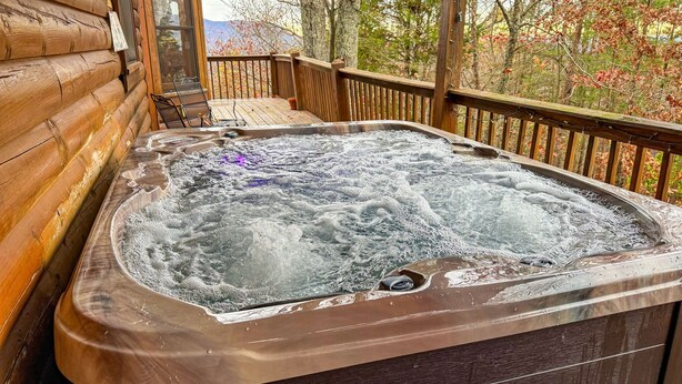Een hottub op een houten terras met uitzicht op bomen en bergen.