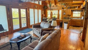 Een gezellig interieur van een chalet met een houten vloer, een bank, een eettafel en een keukenhoek.