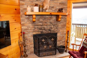A stone fireplace with a mantel shelf, a wooden chair, and a television on the left wall.