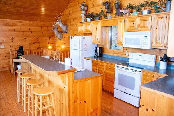 A wooden cabin kitchen with a bar area, wooden cabinets, a refrigerator, a microwave, and a stove. - Mountaintop Experience - Cabin (Sevierville)